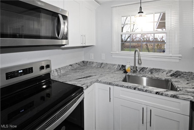 kitchen with sink, appliances with stainless steel finishes, decorative light fixtures, light stone counters, and white cabinetry