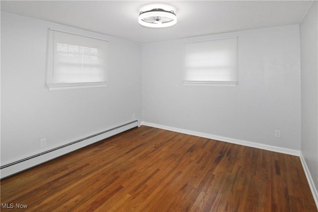 unfurnished room featuring dark wood-type flooring, a wealth of natural light, and a baseboard heating unit