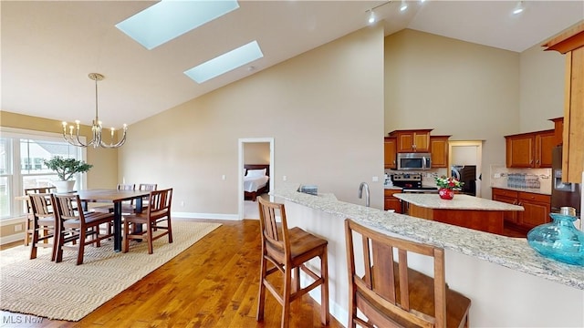 kitchen with a skylight, an inviting chandelier, tasteful backsplash, wood-type flooring, and appliances with stainless steel finishes