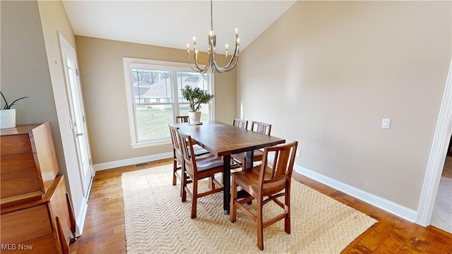 dining room with hardwood / wood-style flooring, vaulted ceiling, and a notable chandelier