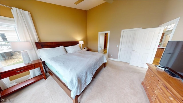 bedroom with light carpet, a towering ceiling, ensuite bath, and ceiling fan