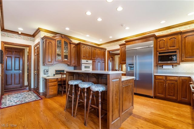 kitchen featuring a breakfast bar area, light countertops, light wood-style floors, glass insert cabinets, and built in appliances