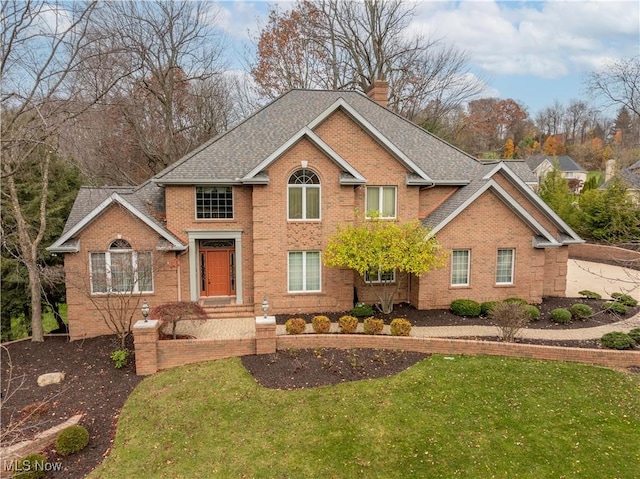 view of front of house with a shingled roof, a front yard, brick siding, and a chimney