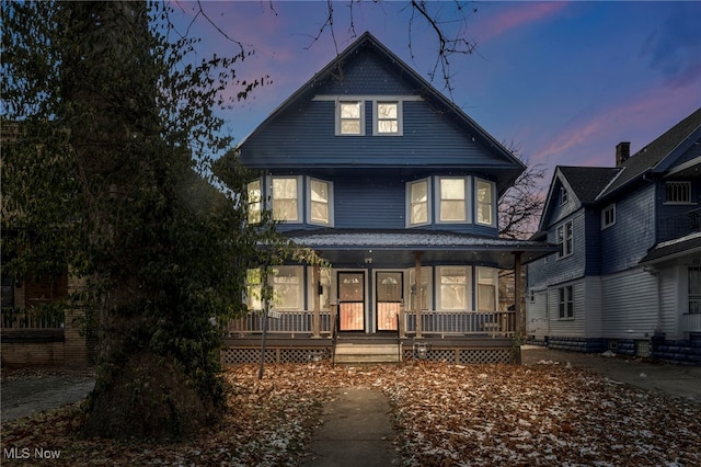 back house at dusk featuring a porch