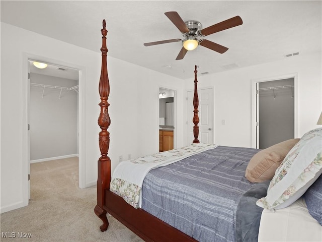 carpeted bedroom featuring ensuite bathroom, ceiling fan, and a walk in closet