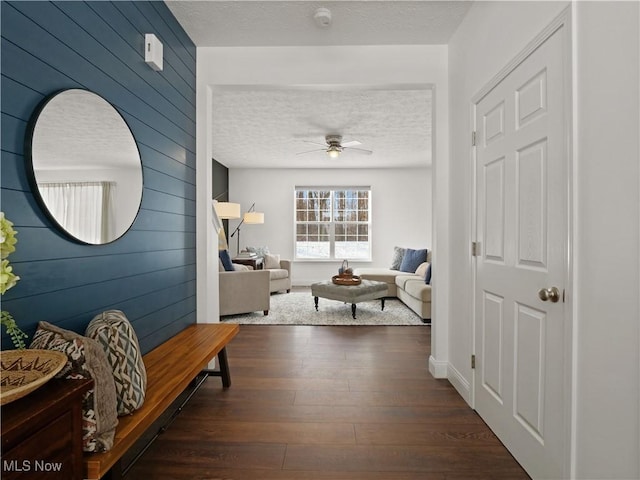 hall featuring a textured ceiling, wood walls, and dark wood-type flooring