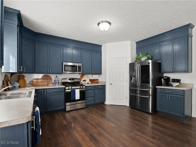 kitchen with sink, blue cabinetry, appliances with stainless steel finishes, and dark wood-type flooring