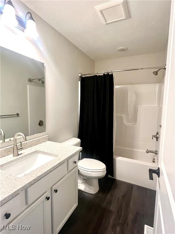 full bathroom featuring hardwood / wood-style floors, vanity, shower / tub combo, and toilet