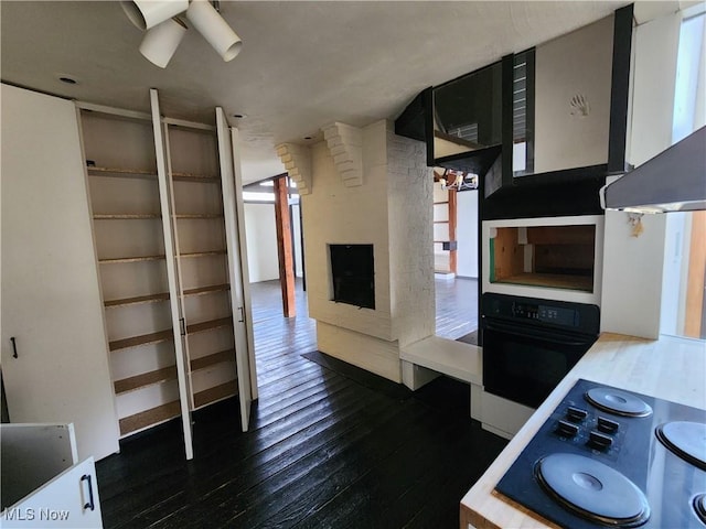 kitchen featuring ceiling fan, dark wood-type flooring, wall chimney range hood, oven, and a fireplace