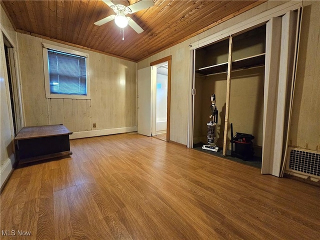 unfurnished bedroom featuring hardwood / wood-style floors, wood walls, wooden ceiling, ceiling fan, and a closet