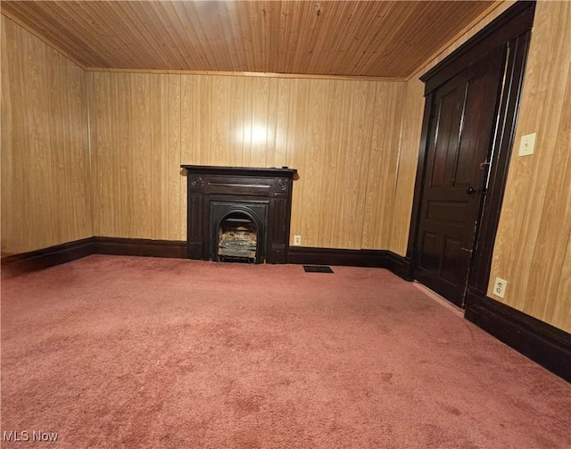 unfurnished living room with carpet, wooden ceiling, a fireplace, and wooden walls