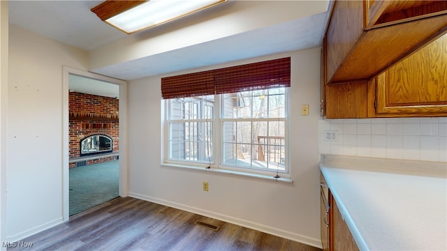 kitchen featuring backsplash, hardwood / wood-style flooring, and a brick fireplace