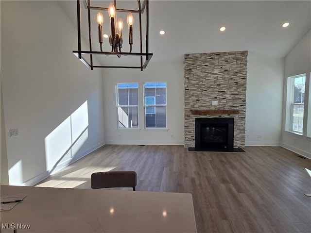 unfurnished living room with hardwood / wood-style floors, a stone fireplace, and a notable chandelier