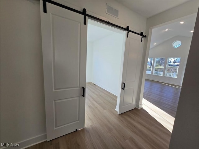 unfurnished room with light wood-type flooring, a barn door, and vaulted ceiling