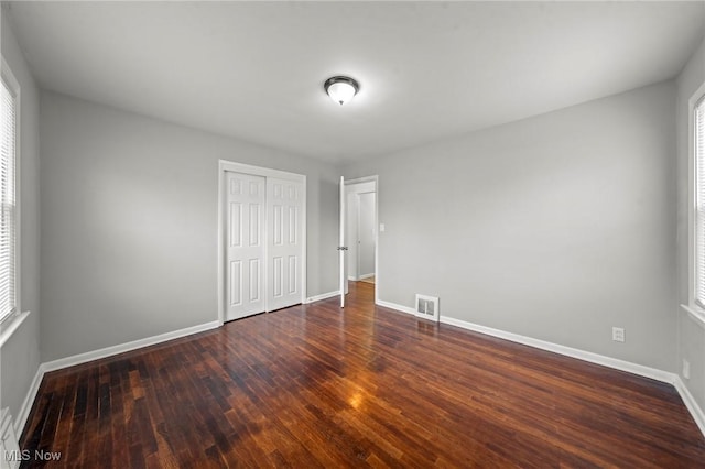 unfurnished bedroom with multiple windows, dark hardwood / wood-style flooring, and a closet