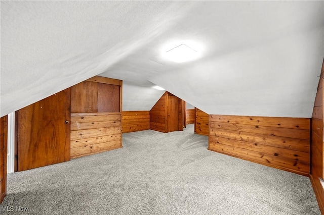 bonus room with a textured ceiling, light carpet, wooden walls, and lofted ceiling