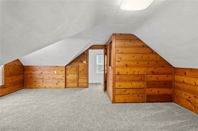 bonus room featuring a textured ceiling, wood walls, lofted ceiling, and light carpet