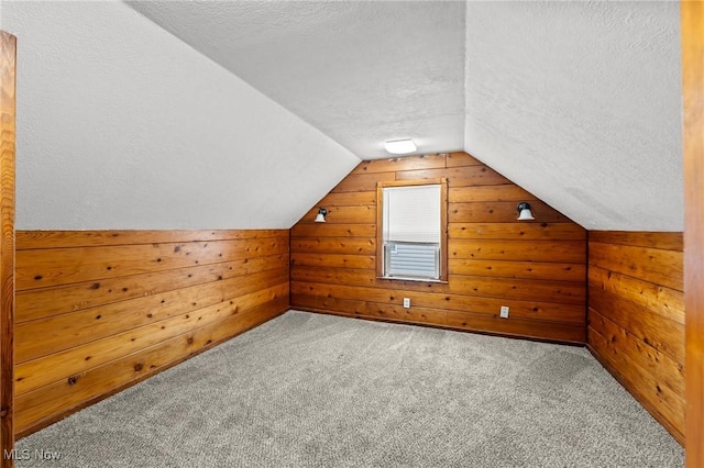 additional living space featuring carpet flooring, a textured ceiling, lofted ceiling, and wood walls