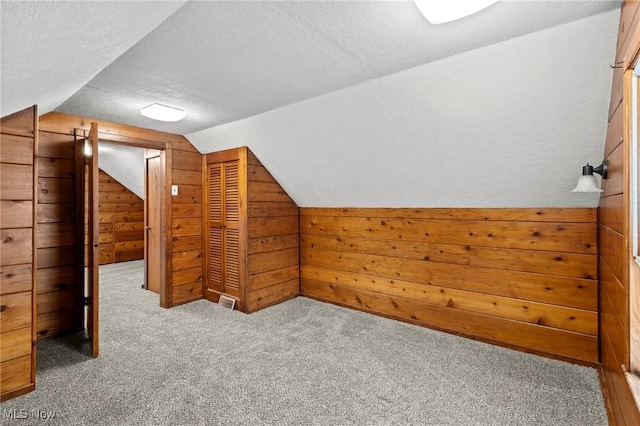 bonus room featuring carpet flooring, a textured ceiling, wooden walls, and vaulted ceiling