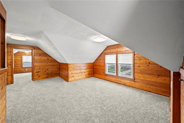 bonus room featuring light carpet, lofted ceiling, and wood walls