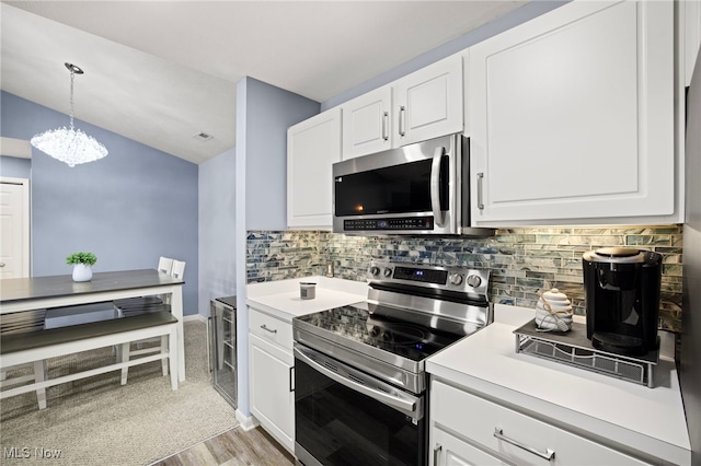 kitchen with appliances with stainless steel finishes, pendant lighting, light hardwood / wood-style flooring, a notable chandelier, and white cabinets