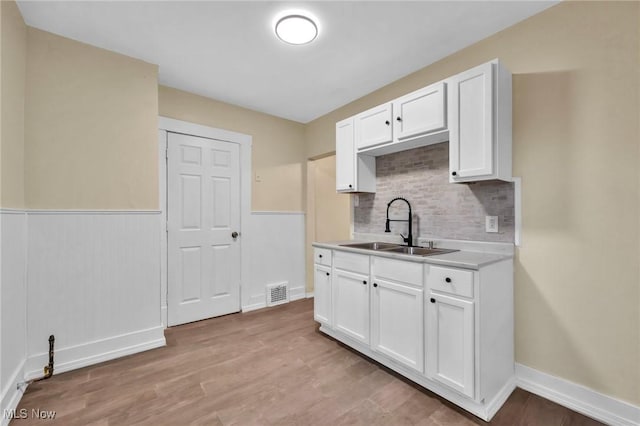 kitchen with white cabinets, decorative backsplash, light hardwood / wood-style flooring, and sink