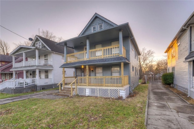 view of front of property featuring a lawn, a balcony, and a porch