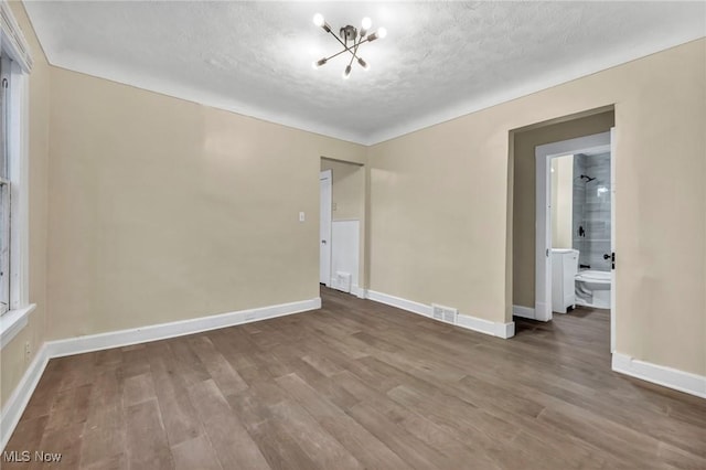 empty room featuring hardwood / wood-style flooring, a notable chandelier, and a textured ceiling