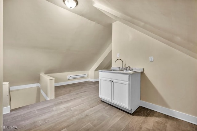 additional living space featuring light wood-type flooring, vaulted ceiling, and sink