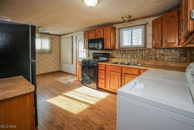 kitchen featuring washer and clothes dryer, crown molding, sink, black appliances, and light hardwood / wood-style flooring