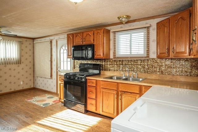 kitchen with black appliances, ornamental molding, sink, and light hardwood / wood-style flooring