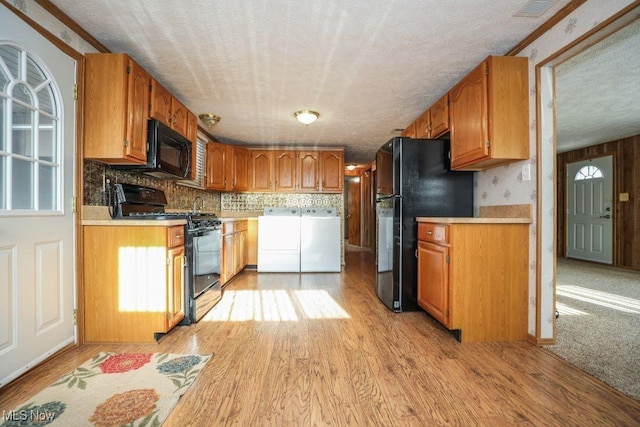 kitchen featuring black appliances, crown molding, light hardwood / wood-style flooring, washer and dryer, and a textured ceiling