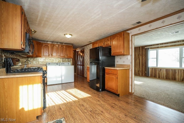 kitchen with washing machine and clothes dryer, a textured ceiling, crown molding, and black appliances