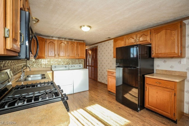 kitchen with black fridge, sink, washing machine and dryer, light hardwood / wood-style floors, and range