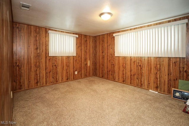 carpeted spare room featuring plenty of natural light and wood walls