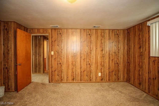 carpeted spare room with a textured ceiling and wooden walls