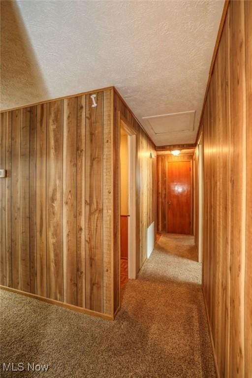 corridor featuring carpet, wood walls, and a textured ceiling