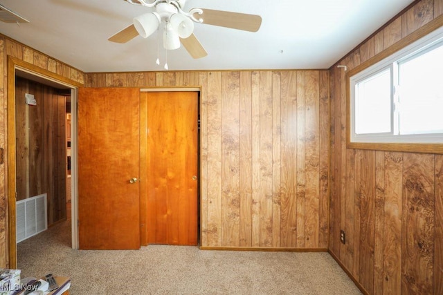 spare room with light carpet, ceiling fan, and wood walls