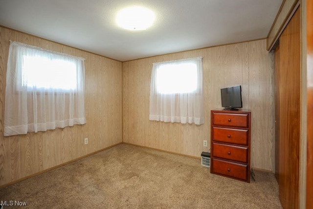 unfurnished bedroom with wooden walls, a closet, and light colored carpet