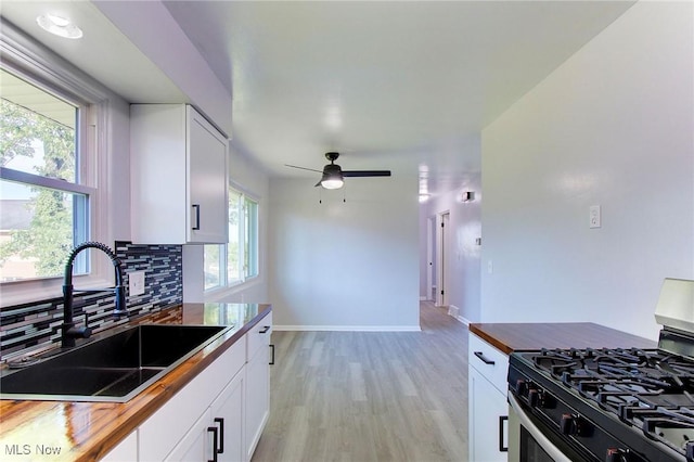 kitchen with white cabinets, stainless steel gas range oven, sink, and wooden counters