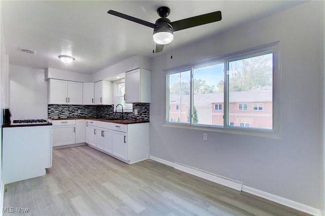 kitchen featuring backsplash, sink, ceiling fan, a baseboard radiator, and white cabinetry