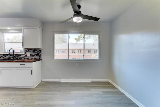 kitchen featuring decorative backsplash, light wood-type flooring, ceiling fan, sink, and white cabinetry