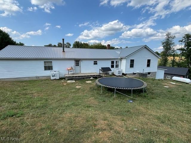 rear view of property with a yard, a trampoline, and a deck