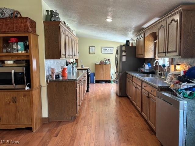 kitchen with lofted ceiling, backsplash, a textured ceiling, light hardwood / wood-style floors, and stainless steel appliances