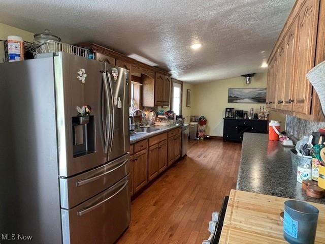 kitchen with stainless steel fridge, a textured ceiling, vaulted ceiling, dark wood-type flooring, and sink