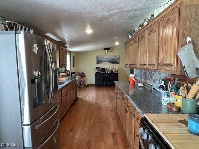 kitchen featuring backsplash, dark wood-type flooring, stainless steel refrigerator with ice dispenser, vaulted ceiling, and a textured ceiling