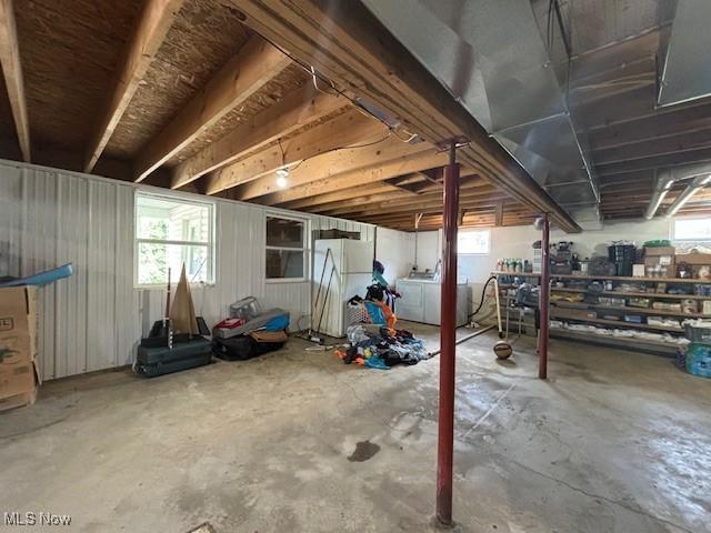 basement featuring white fridge, a wealth of natural light, and washing machine and clothes dryer