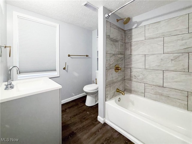 full bathroom with tiled shower / bath combo, wood-type flooring, a textured ceiling, toilet, and vanity