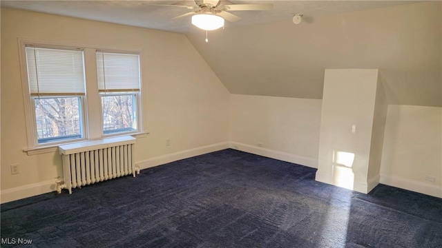 additional living space with dark colored carpet, ceiling fan, radiator, and vaulted ceiling