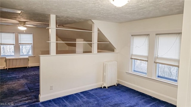 spare room with dark colored carpet, plenty of natural light, and radiator